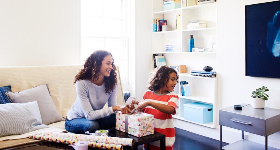 Mother and daughter wrapping gifts, interacting with voice assistant