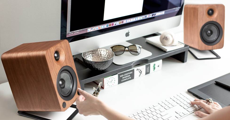 A person working at a computer on a desk, with Kanto YU4 desktop speakers.