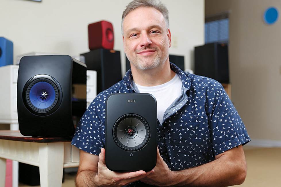 Man holding KEF LSX speakers in his home