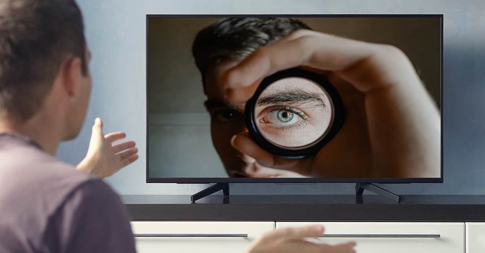 A man watching at TV. On the TV is a man looking back at the viewer.