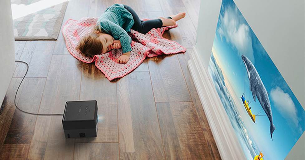 A small child lying on a blanket on the floor next to a EpiqVision projector