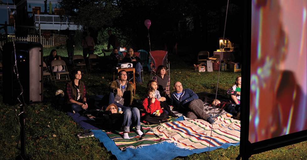 A family outdoors watching a movie in their backyard