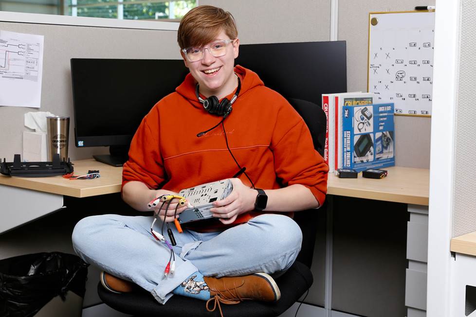 Friendly Crutchfield tech support person, sitting at their desk holding a car stereo receiver.