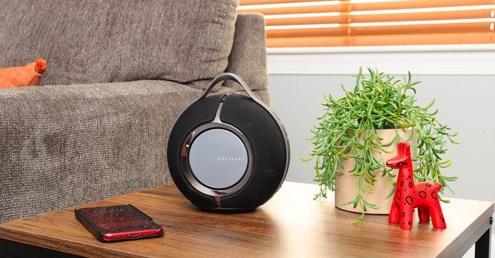 Devialet Mania Portable Bluetooth® speaker sitting on an end table next to a sofa.