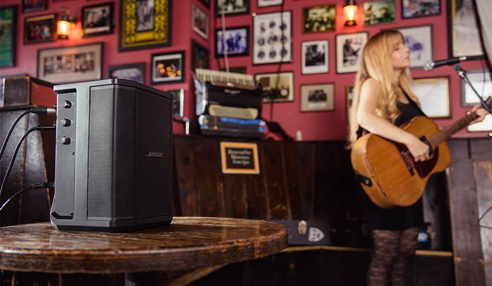 Woman playing guitar in a bar or coffee shop with a Bose portable PA speaker