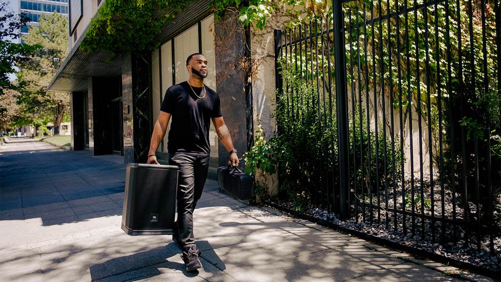 Person carrying a PA speaker walking along a city sidewalk