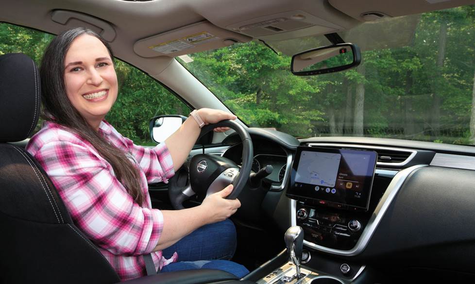 Photo of Natalie wearing a pink plaid shirt, sitting in Her Nissan Murano.
