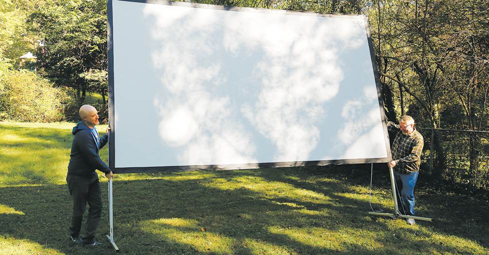 Two people setting up an outdoor projector screen.