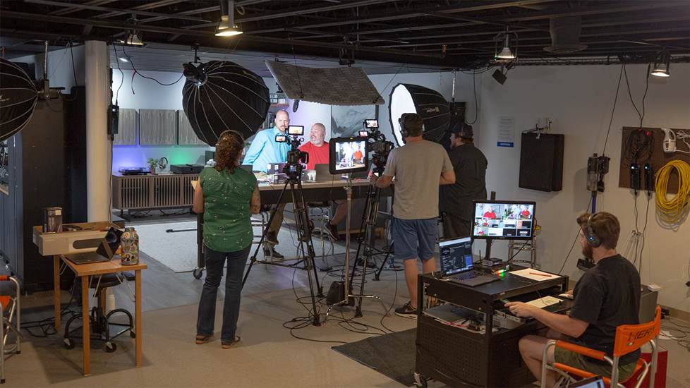 Behind the scenes in a video studio showing on camera talent and production crew