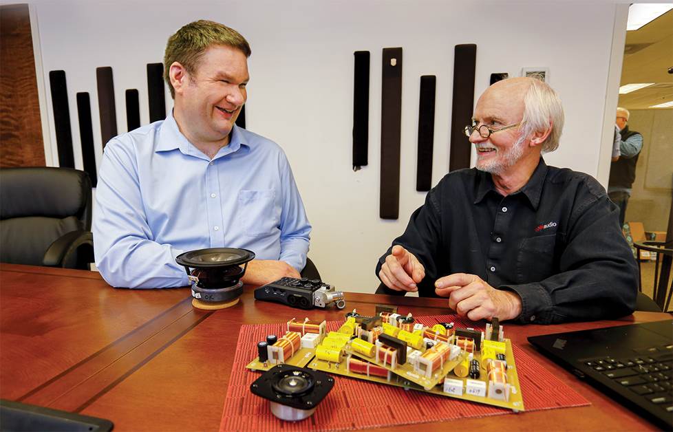 Two men sitting at a table with speaker components