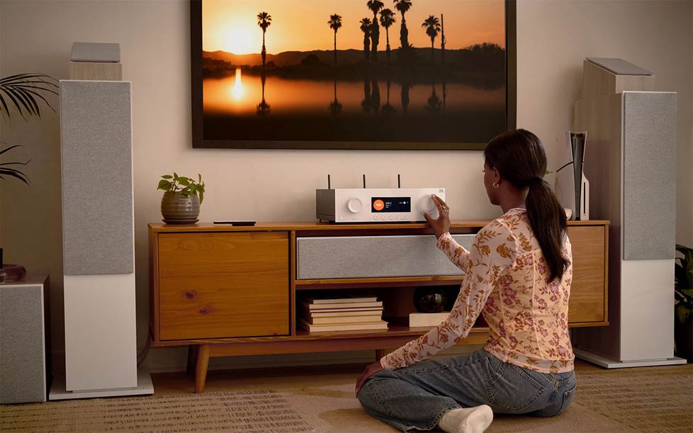 Woman adjusting JBL MA7100W receiver connected to a surround sound system and a TV.