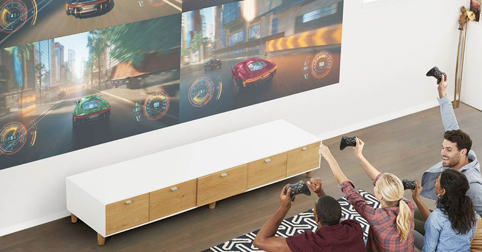 four people sitting on a sofa with video game controllers playing a racing game on the screen